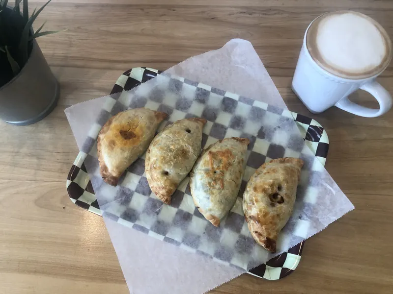 Four baked empanadas on a checkered paper tray next to a latte