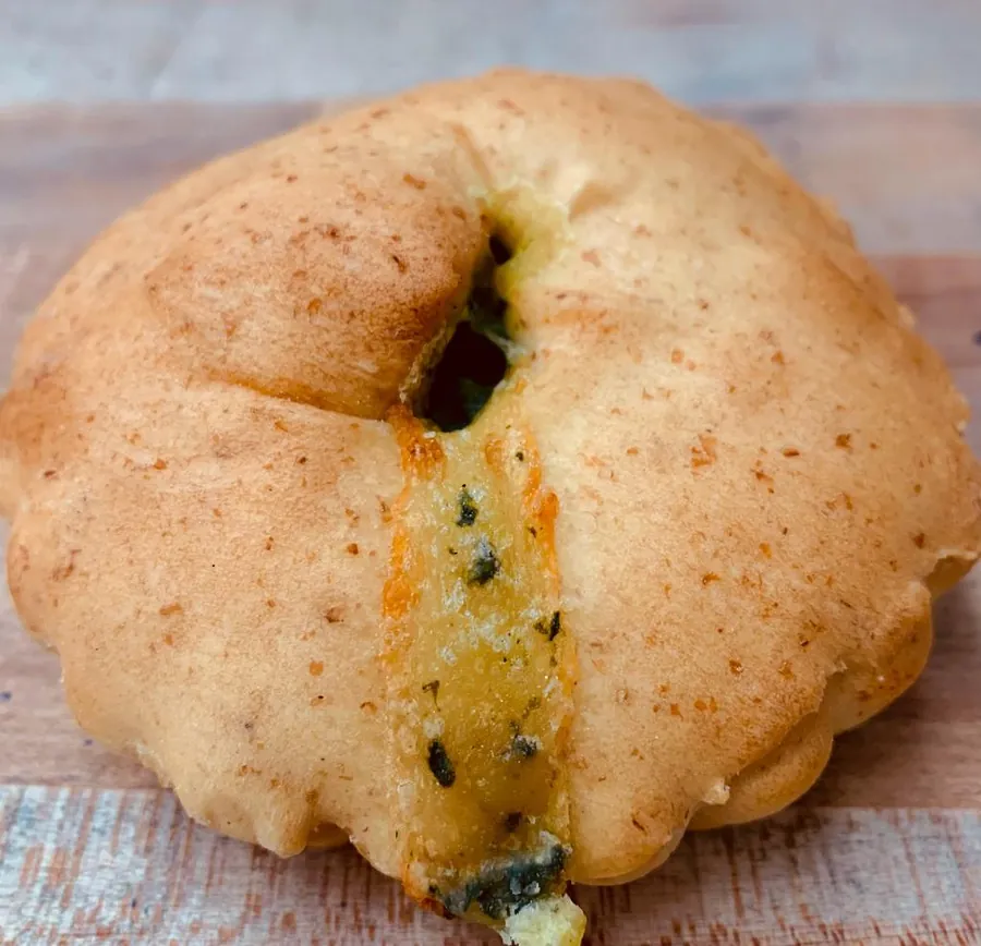A whole round pie with a green, cheesy filling peeking from a slit
