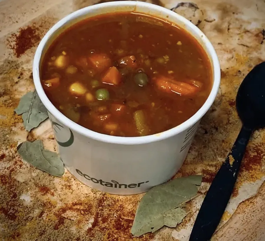 A cup of vegetable soup with carrot, peas and corn on a wooden board