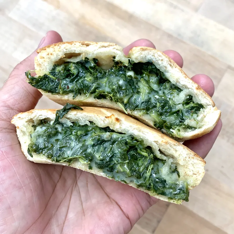 Hand holding a cut pie with a spinach and cheese filling